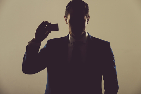 A business man in shadow holding a business card